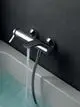 Wandmontierte Badearmatur aus verchromtem Metall von Ideal Standard, mit einem Auslauf, der Wasser in eine Badewanne leitet, an einer dunklen Wand installiert.